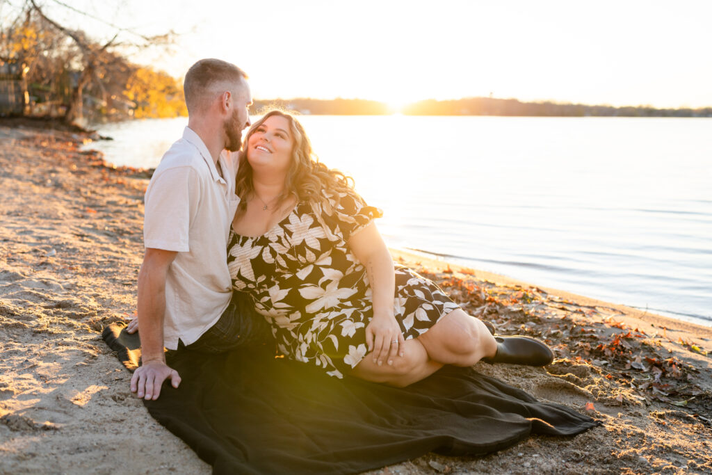 A couple sitting on a beach during golden hour, sharing a romantic moment knowing they already have booked their venue.
