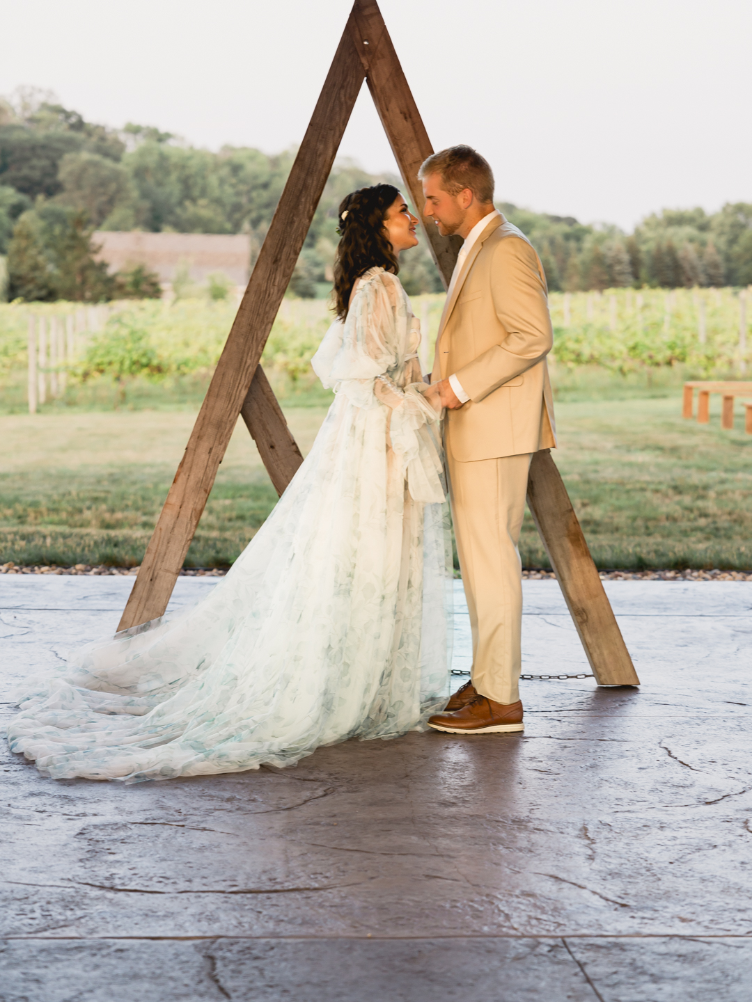 Bride and groom standing under a wooden arch in a vineyard during their Atlanta outdoor wedding ceremony.