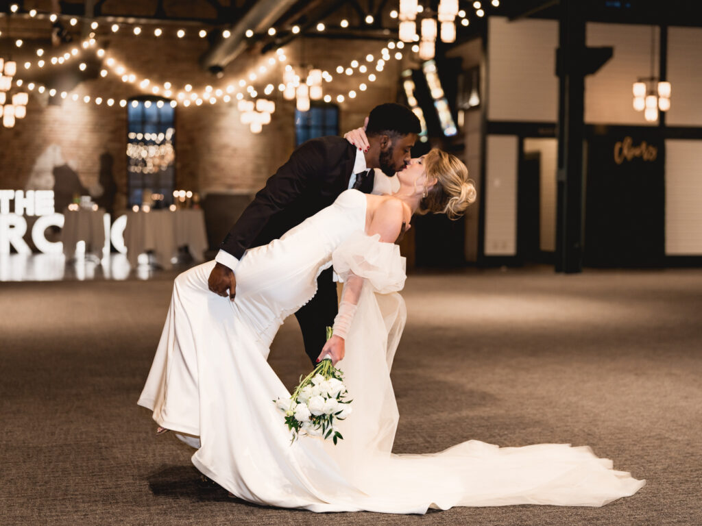 Bride and groom sharing a romantic dance under string lights at an Atlanta indoor wedding venue.