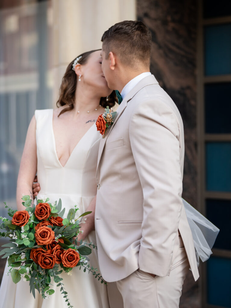 Bride and groom sharing a kiss with a rust-colored bouquet at their elegant Atlanta wedding.