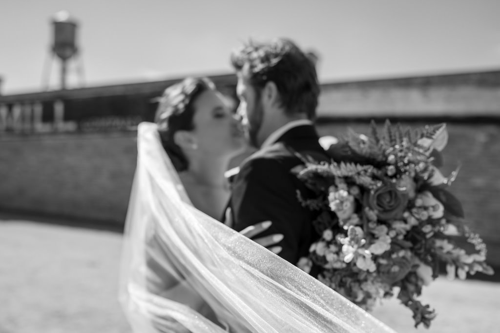 Bride and groom with veil in motion in front of Walton Mill.