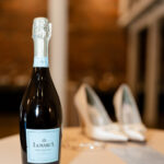 La Marca Prosecco bottle and elegant bridal heels on a table at The Factory at Walton Mill, captured as a getting ready wedding detail.