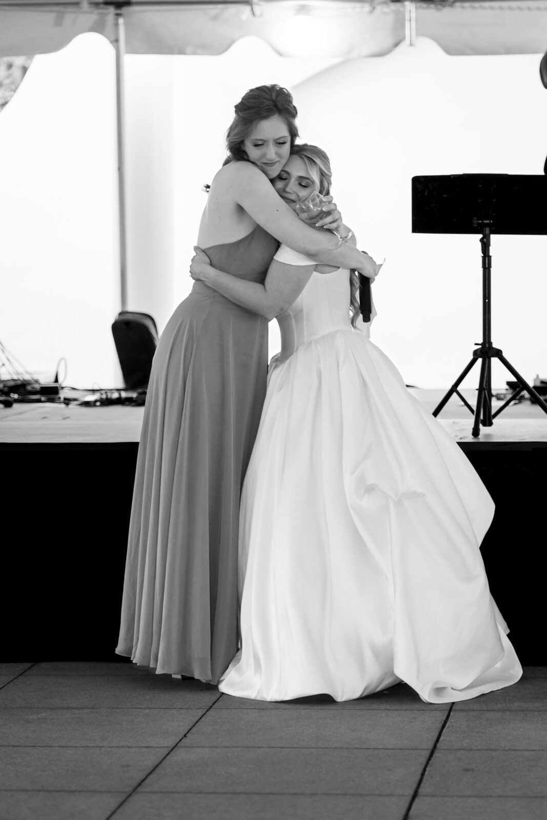 The bride and maid of honor share a tight embrace after a moving toast under the tented reception space.