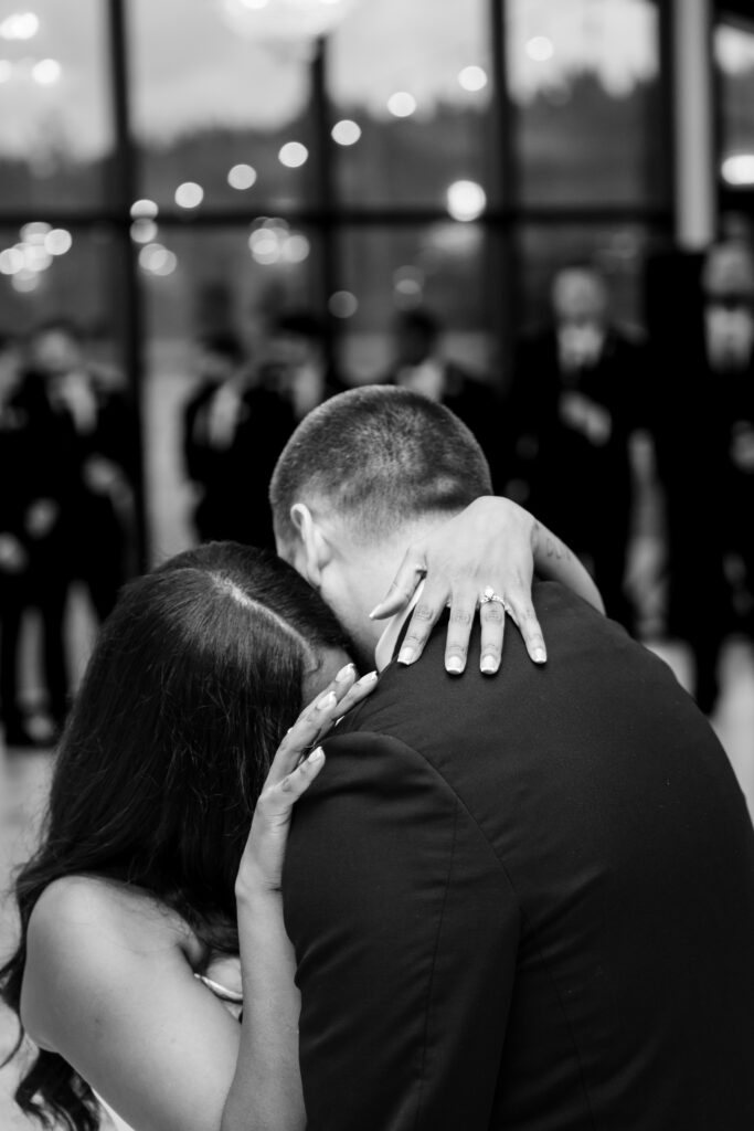Intimate black and white portrait of bride holding onto groom during a quiet dance moment.