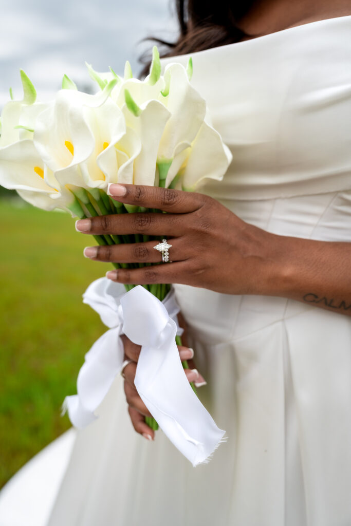 Close-up of bride’s hands, bouquet, and engagement ring with soft light and elegant ribbon.