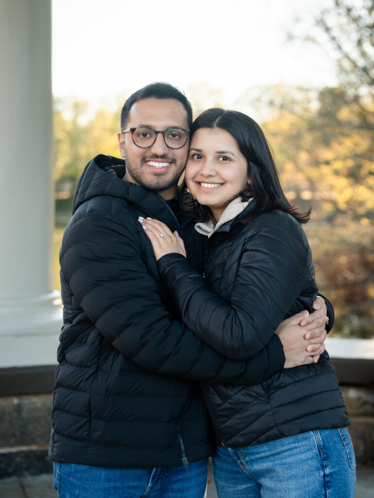 Newly engaged couple hugging and smiling by the lake in Piedmont Park, Atlanta, with autumn trees in the background.