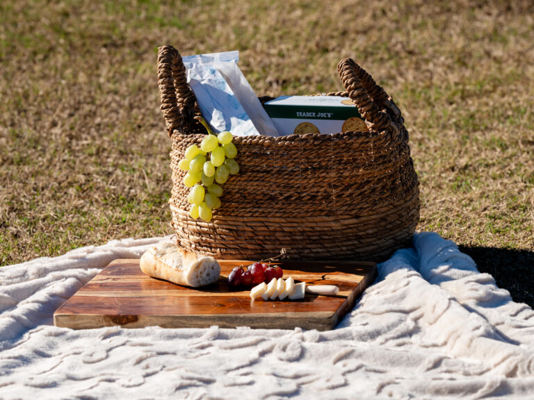 Picnic proposal setup on a cream blanket with a woven basket, bread, cheese, and grapes in Piedmont Park, Atlanta.