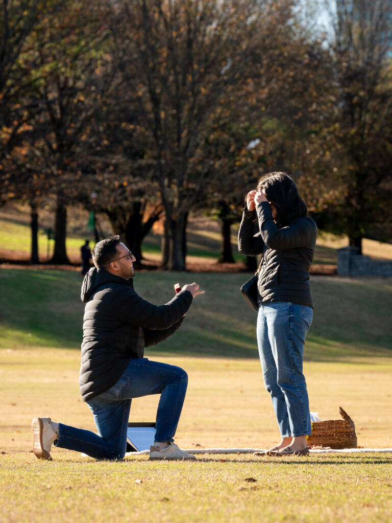 Piedmont Park proposal photo as he presents the ring box during the surprise proposal in The Meadow.