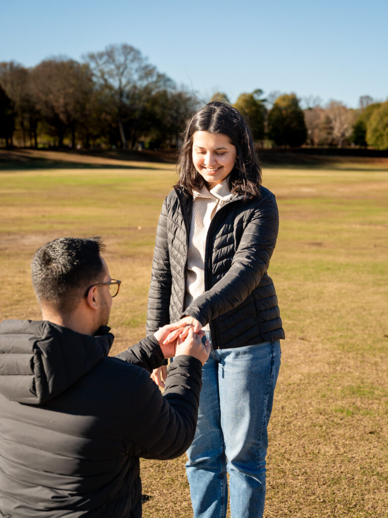 Man kneeling to propose while holding his partner’s hand on an open field in Piedmont Park, Atlanta, during golden afternoon light.