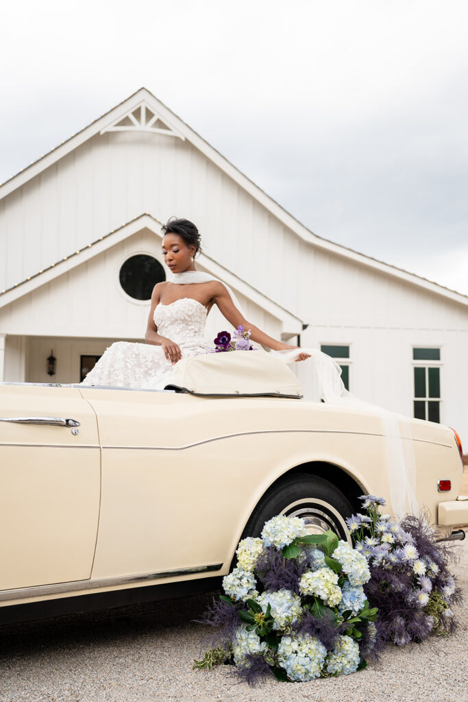 Average Wedding Cost Georgia | Kalyn Wolf Studios Bride sides in vintage car outside a wedding venue with purple and blue florals on the ground, reflecting average cost of a wedding in Georgia.